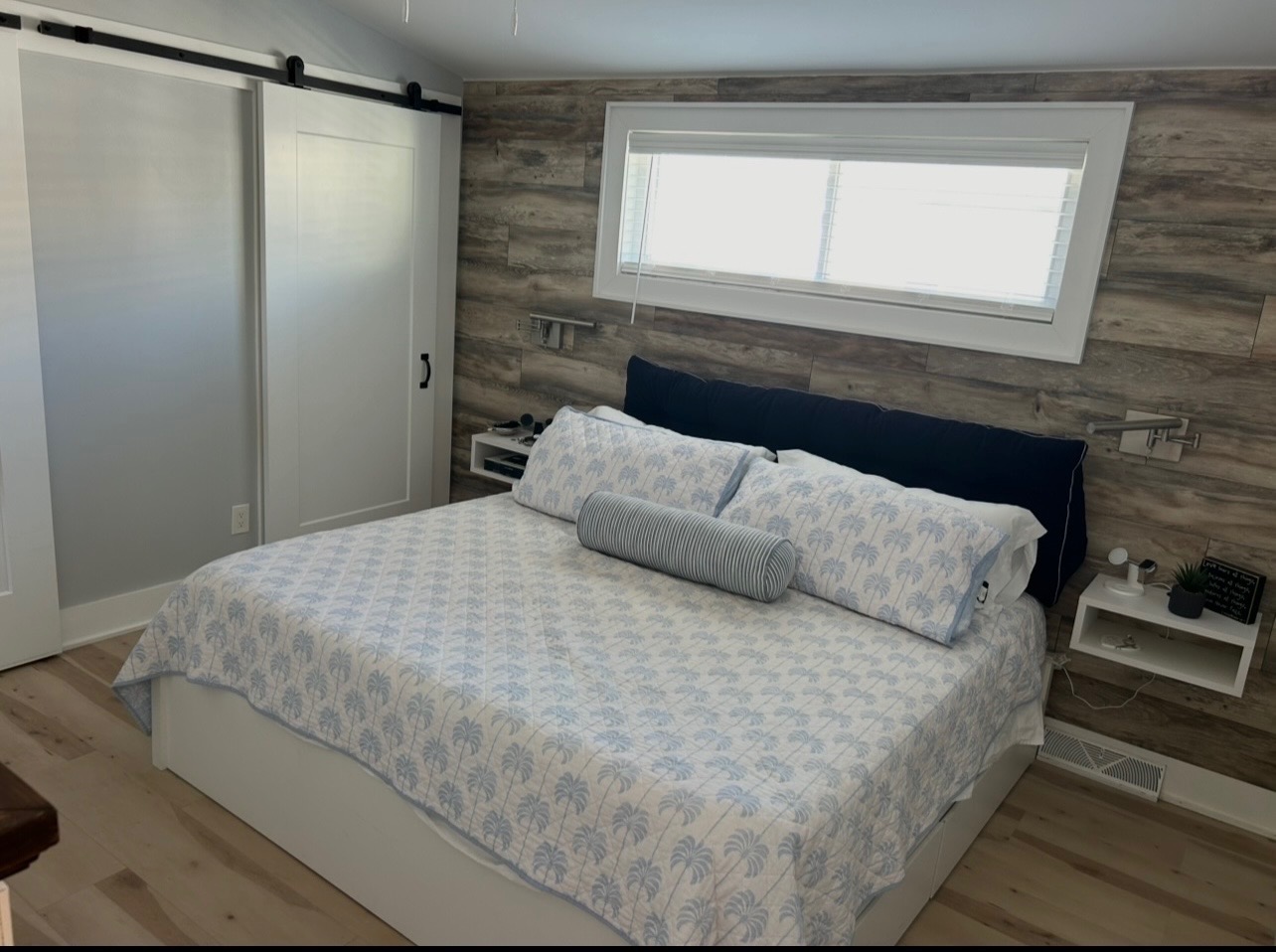 King bedroom with palm-print bedding and wood accent wall